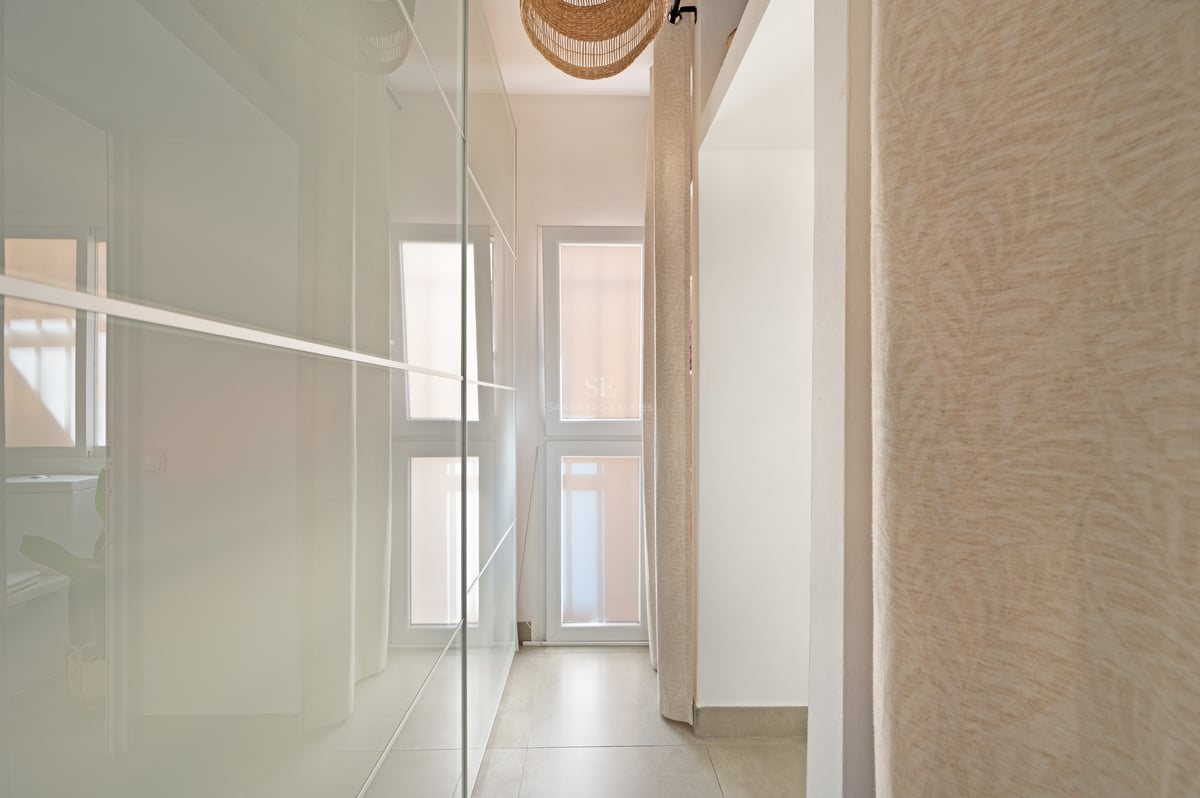 Couloir avec placards de plain-pied en verre dépoli, carrelage beige et suspension en osier.