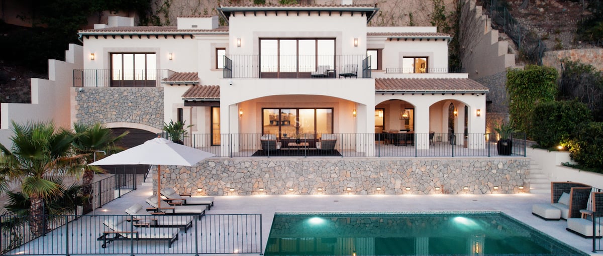 Vue de face d'une villa blanche à deux étages au crépuscule avec piscine et transats au premier plan.