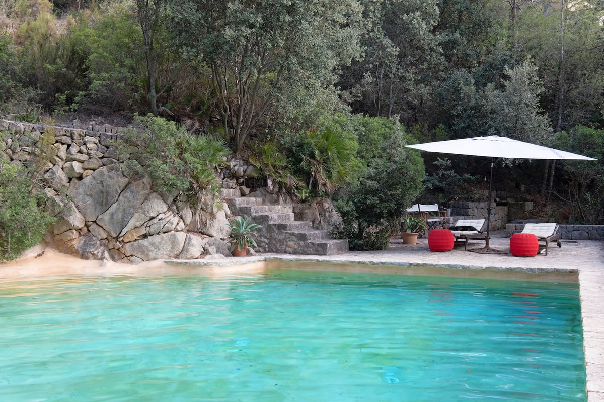 Piscine aux eaux turquoise nichée contre une paroi rocheuse naturelle avec des escaliers en pierre et une végétation dense.