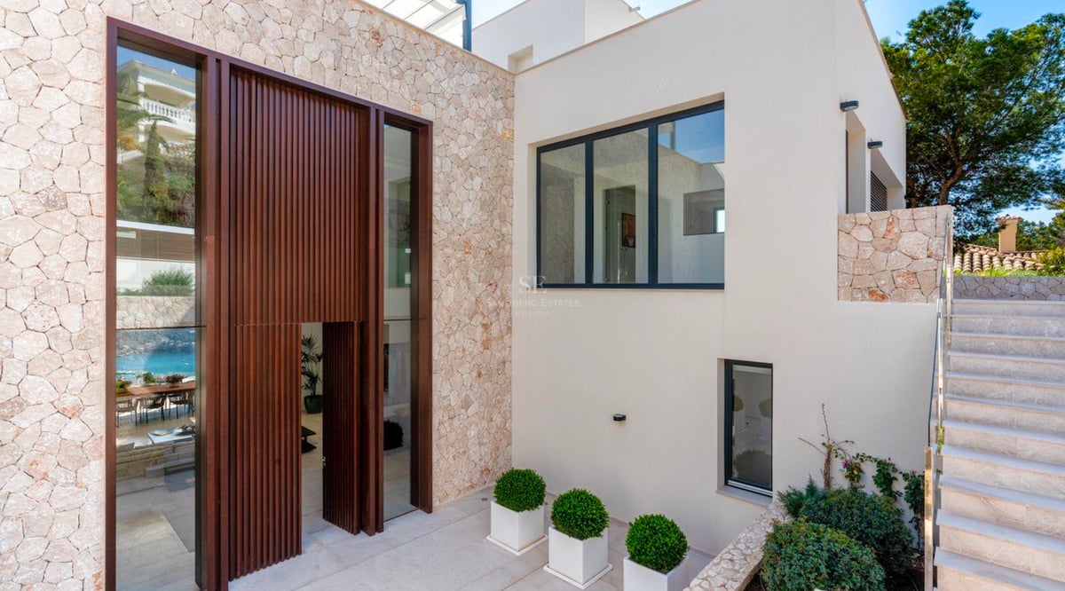 Entrée de villa moderne avec une haute porte en bois à lattes, des murs en pierre naturelle et un extérieur blanc.