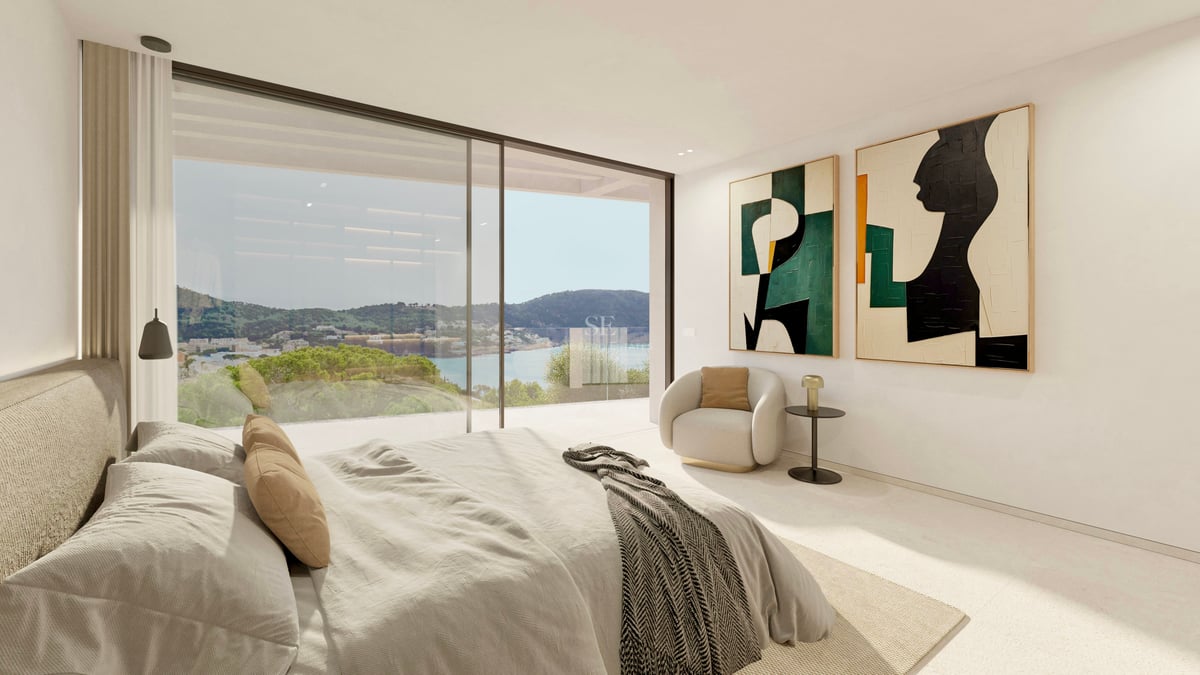 Chambre parentale moderne avec grandes baies vitrées donnant sur un paysage côtier, art abstrait et fauteuil.