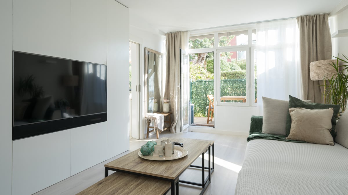 Salon moderne avec meuble TV blanc, table basse en bois et porte vitrée donnant sur une terrasse privée.