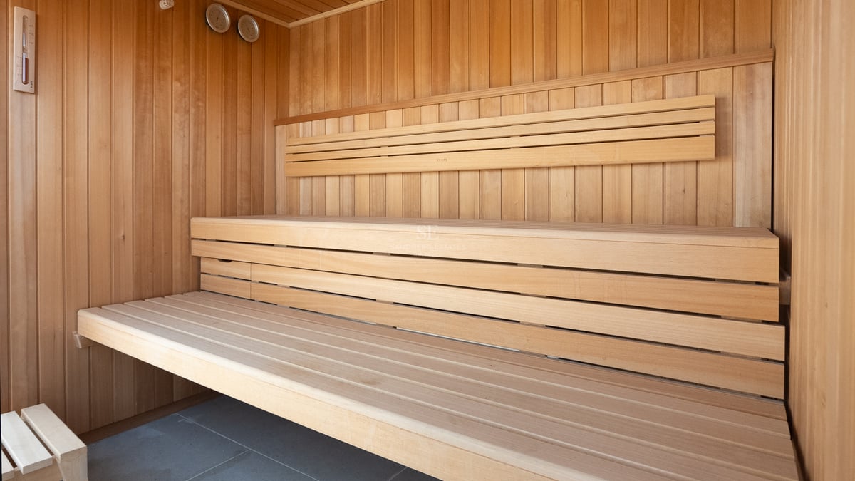 Sauna moderne en bois avec bancs à plusieurs niveaux et jauges de température intégrées sur un sol en pierre grise.
