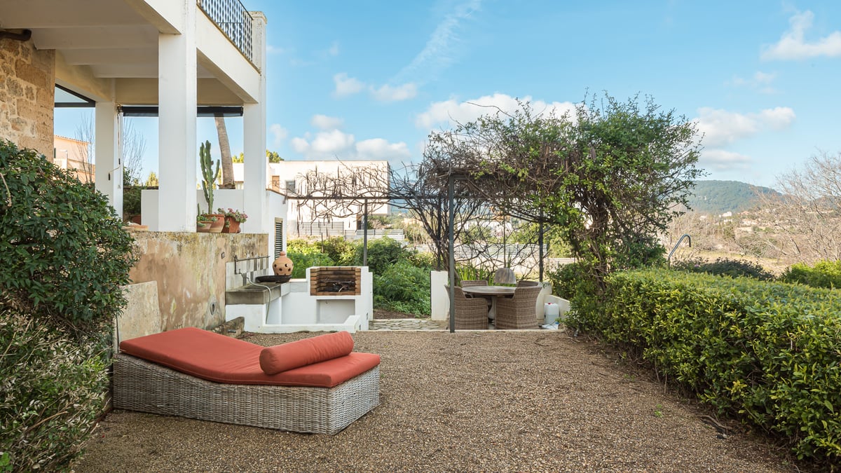 Terrasse avec bain de soleil orange, barbecue maçonné et coin repas sous une pergola verdoyante.