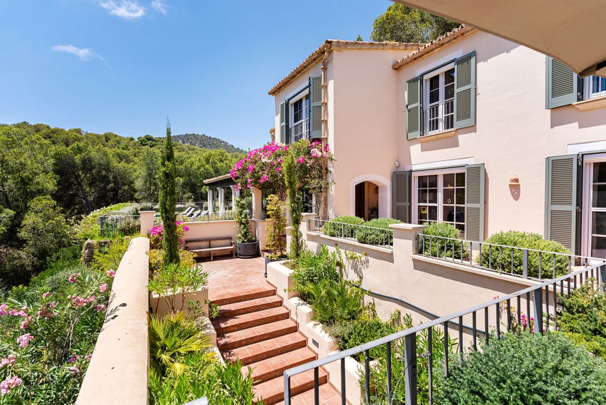 Villa couleur pêche avec volets verts et terrasse en terre cuite surplombant une vallée boisée ensoleillée.