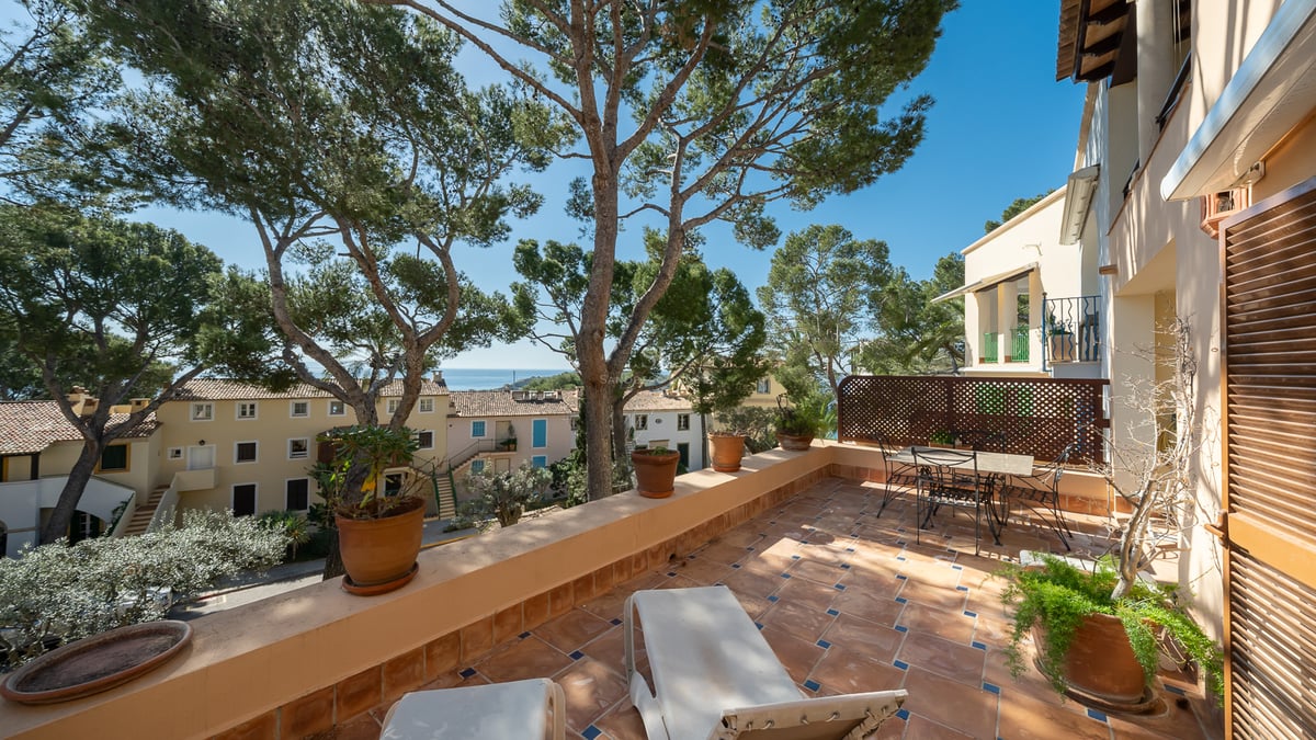 Terrasse en terre cuite avec chaises longues et table, surplombant des pins et la mer sous un ciel bleu.