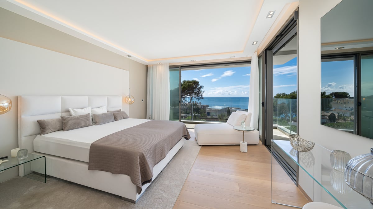 Chambre principale contemporaine avec grand lit, parquet en bois et baies vitrées offrant une vue panoramique sur la mer.
