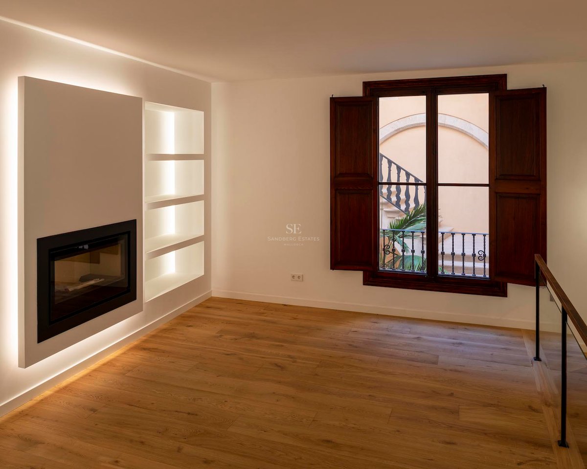 Pièce moderne vide avec cheminée intégrée, étagères rétroéclairées, parquet en chêne et volets en bois foncé.