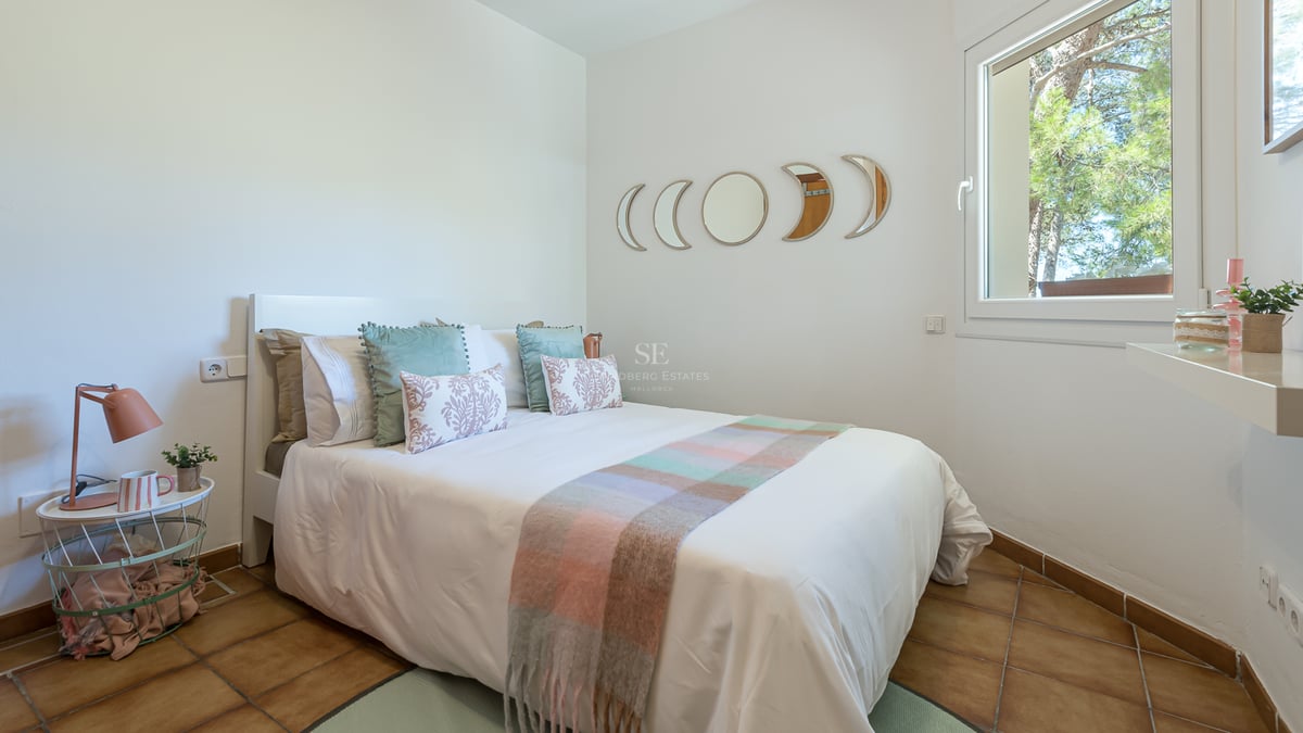 Chambre avec lit blanc, sol en terre cuite et miroirs phases de lune au-dessus de la tête de lit.