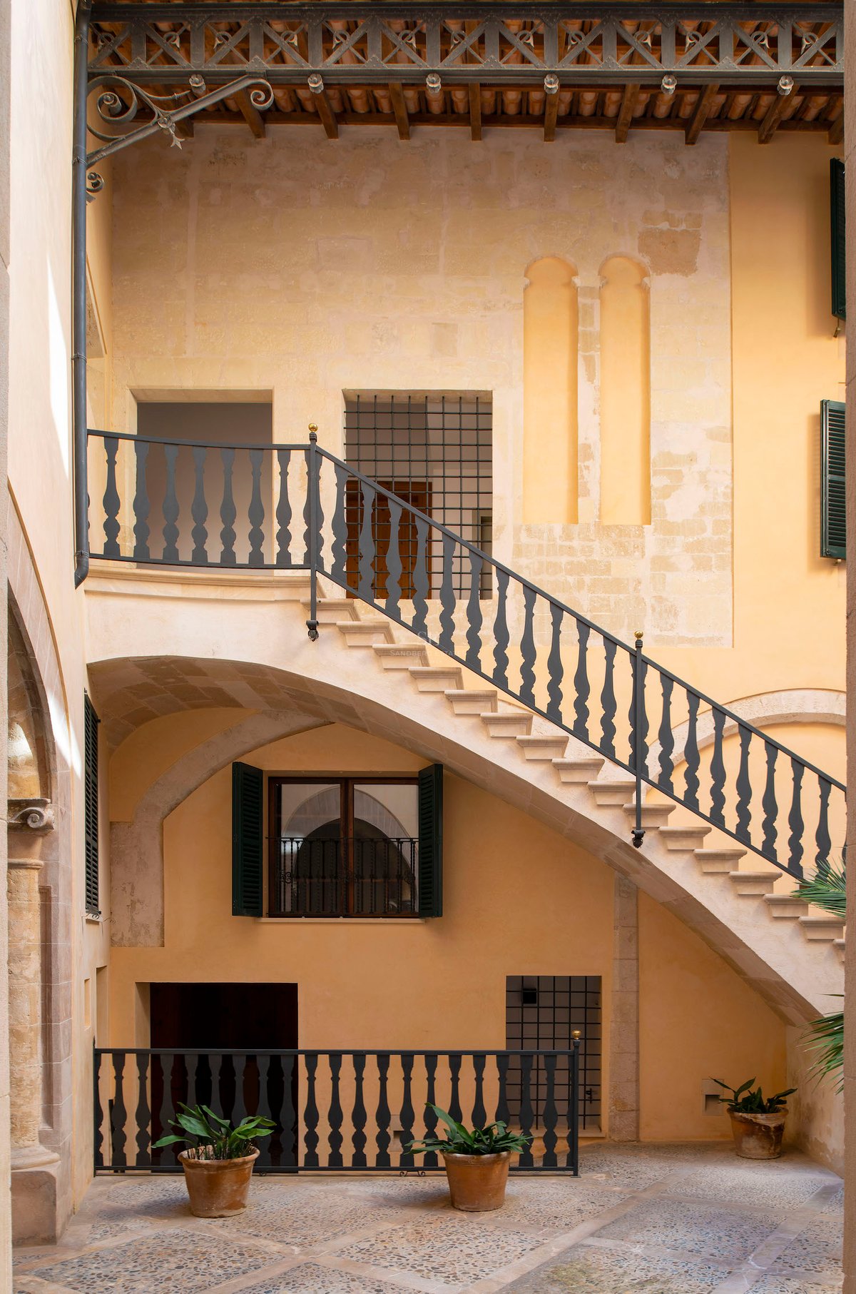 Cour intérieure avec un escalier en pierre, des rampes en fer forgé et des murs ocre chaleureux.