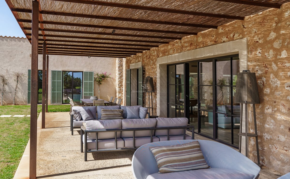 Zona de estar exterior techada con sofás modernos, pared de piedra rústica y techo de vigas de madera.