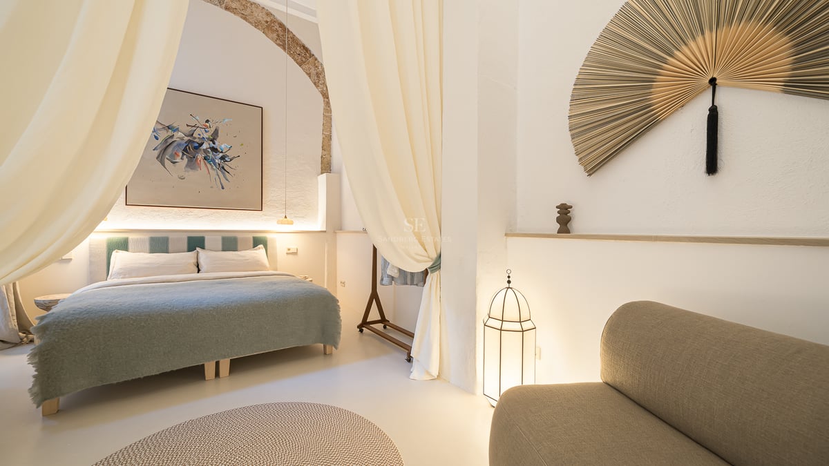 Chambre élégante avec grand lit, rideaux fluides, arche en pierre et décoration artistique.