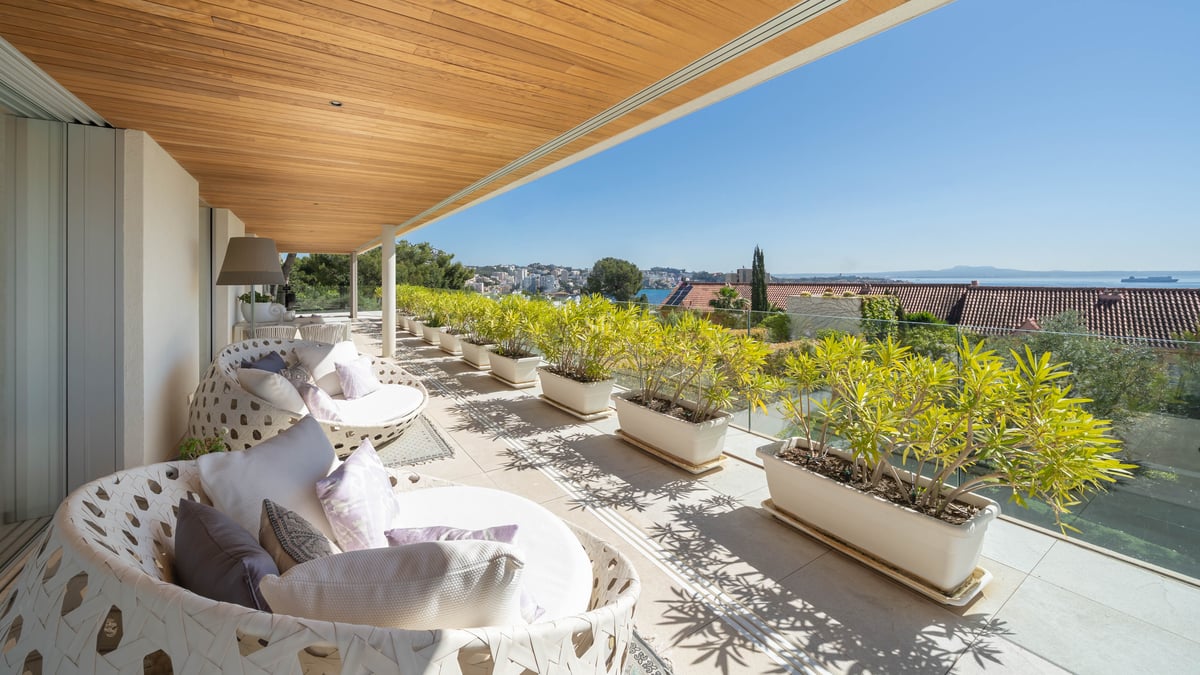 Terrasse moderne couverte avec plafond en bois, mobilier blanc et jardinières donnant sur la mer.