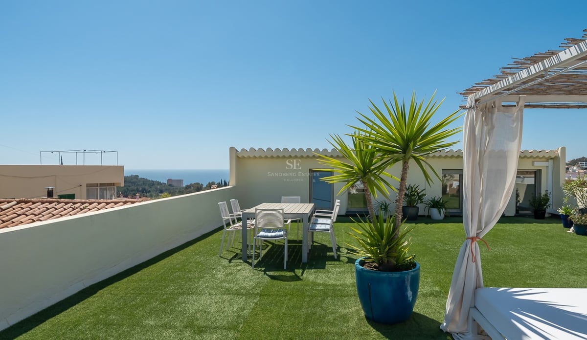 Toit-terrasse avec gazon synthétique, espace repas et lit de repos surplombant la mer Méditerranée.