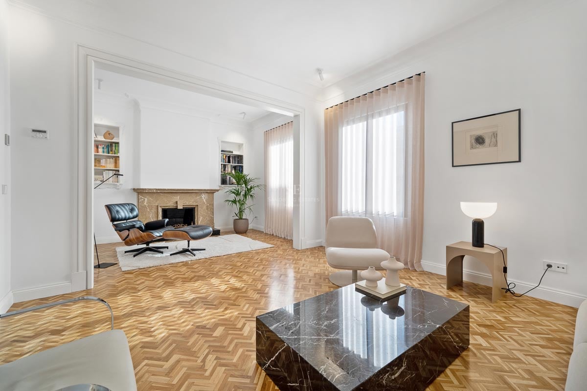 Salon lumineux avec parquet en chevrons, table basse en marbre noir et fauteuil Eames près d'une cheminée.