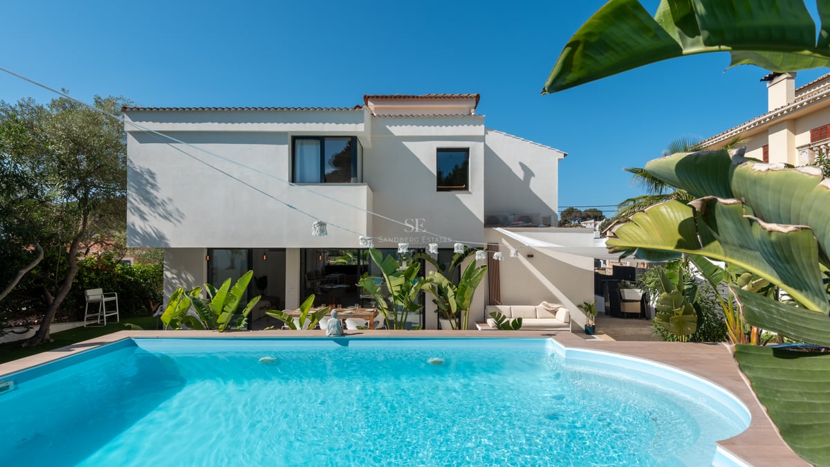 Piscine turquoise devant une villa contemporaine blanche entourée de palmiers sous un ciel bleu azur.