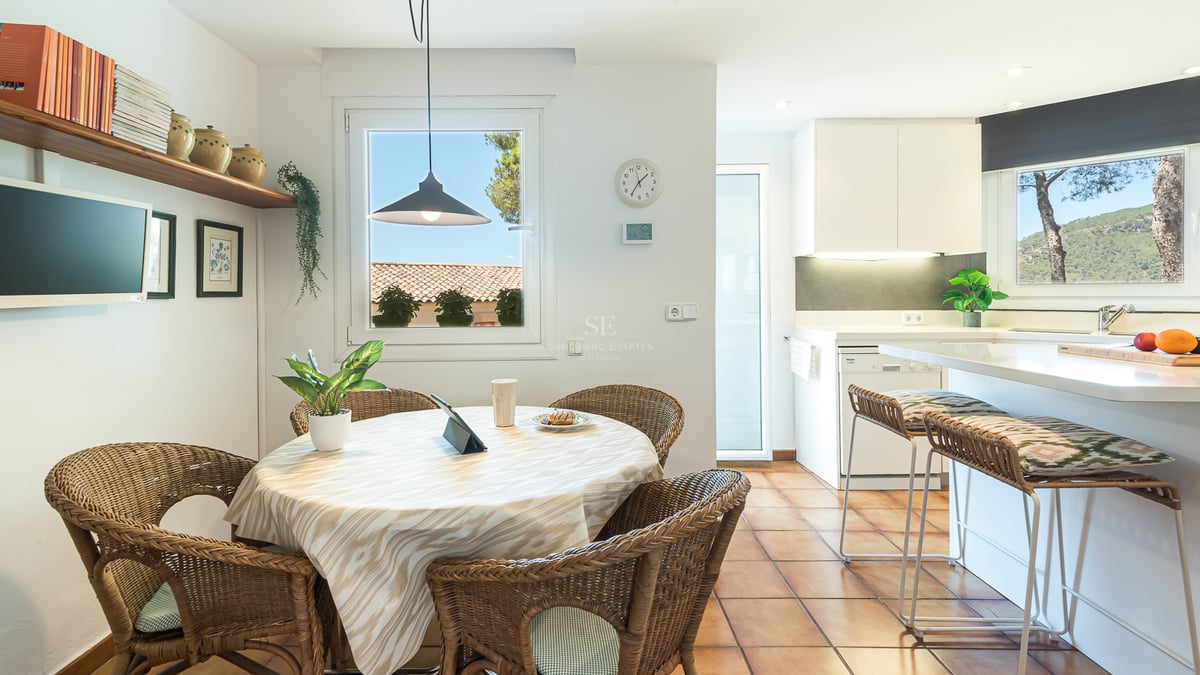 Table à manger ronde avec chaises en osier et sol en terre cuite à côté d'une cuisine moderne blanche.