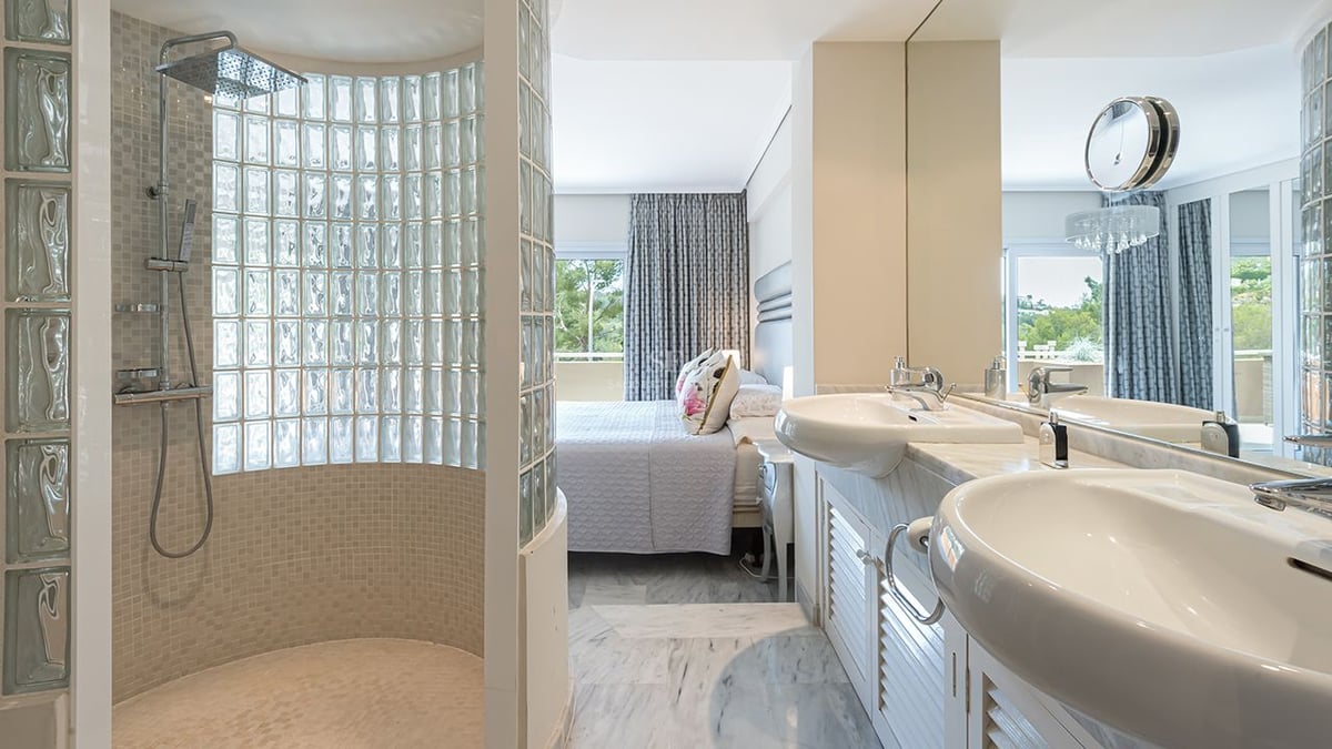 Salle de bains attenante avec double vasque en marbre et douche en briques de verre, ouverte sur la chambre.
