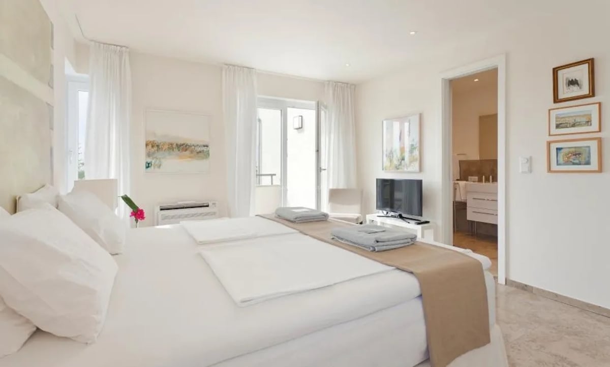 Chambre principale moderne blanche avec salle de bain attenante, sol en marbre et accès terrasse.