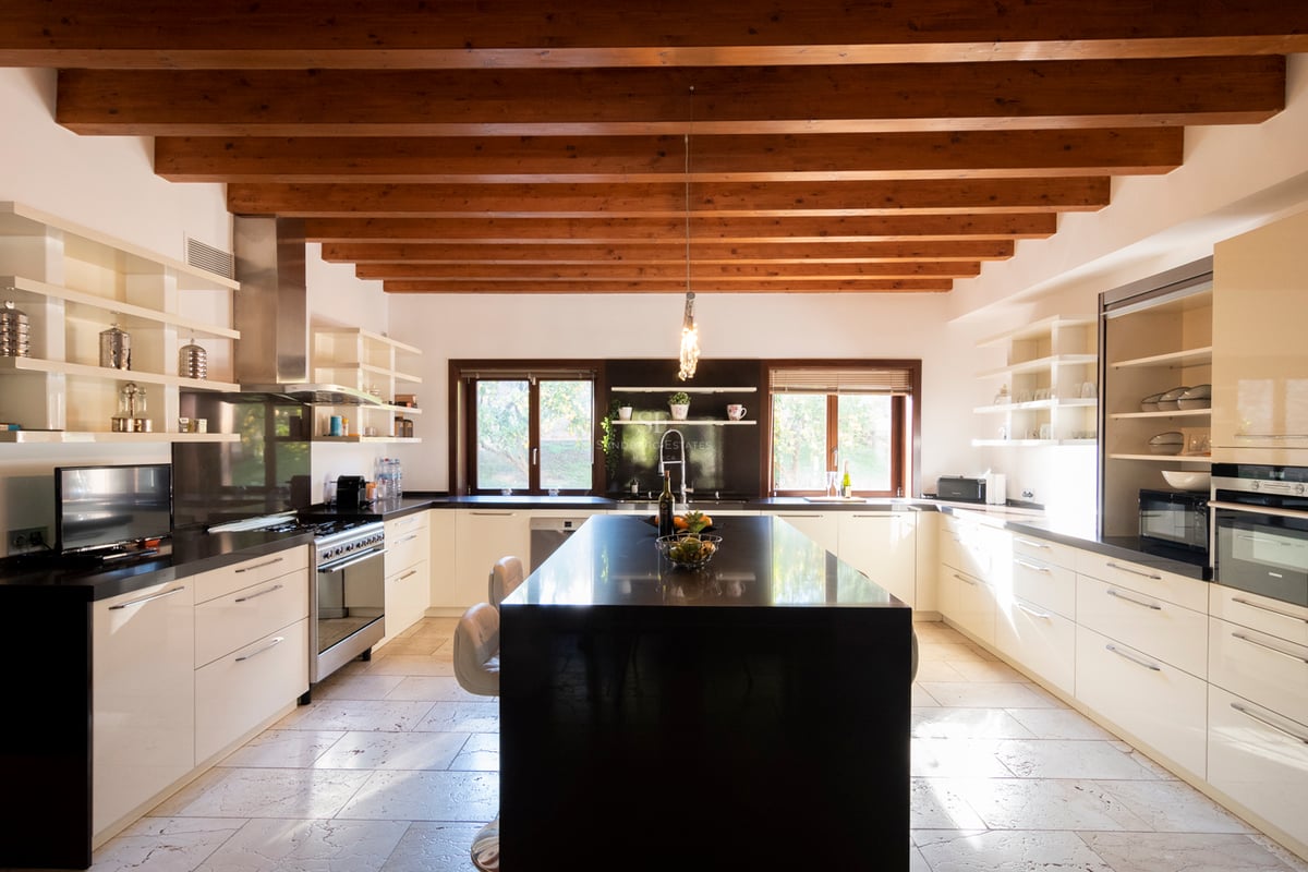 Grande cuisine moderne avec placards blancs, îlot en granit noir et plafond à poutres de bois traditionnelles.