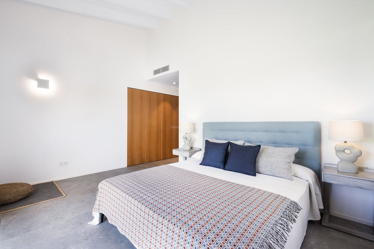 Chambre lumineuse avec un grand lit, tête de lit bleu clair, lampes design et armoire encastrée en bois.