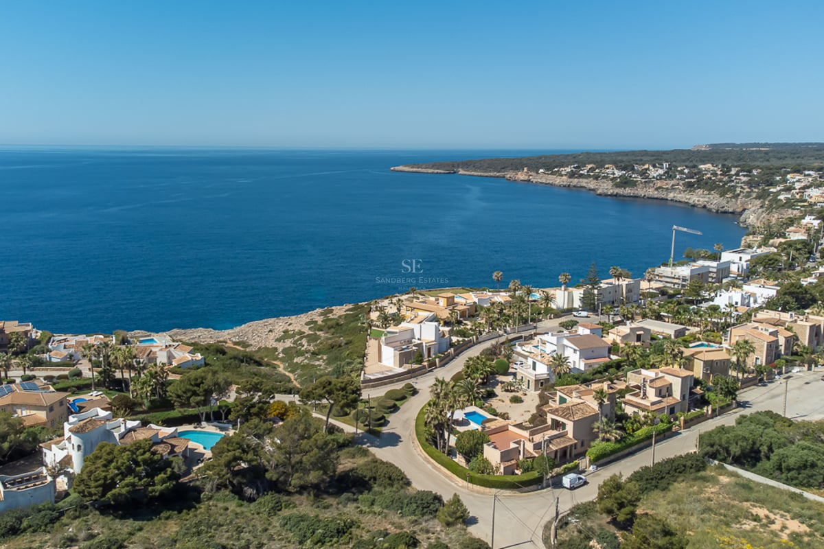 Vue aérienne de villas blanches de luxe avec piscines bleues le long d'une côte méditerranéenne rocheuse.