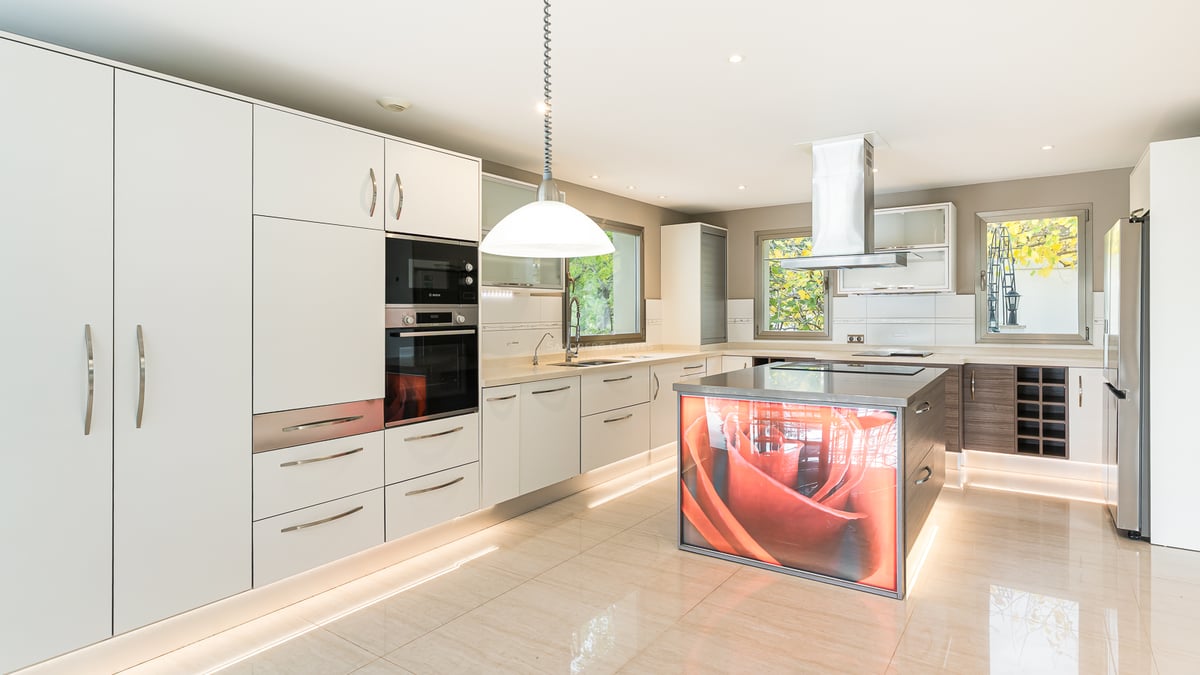 Cuisine blanche moderne avec électroménager en inox et un îlot central rétroéclairé affichant une rose orange.