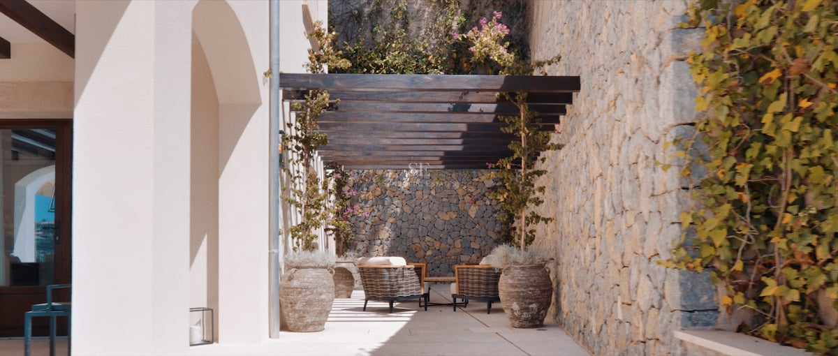 Terrasse méditerranéenne ensoleillée avec murs en pierre rustique, pergola en bois sombre et sièges extérieurs confortables.