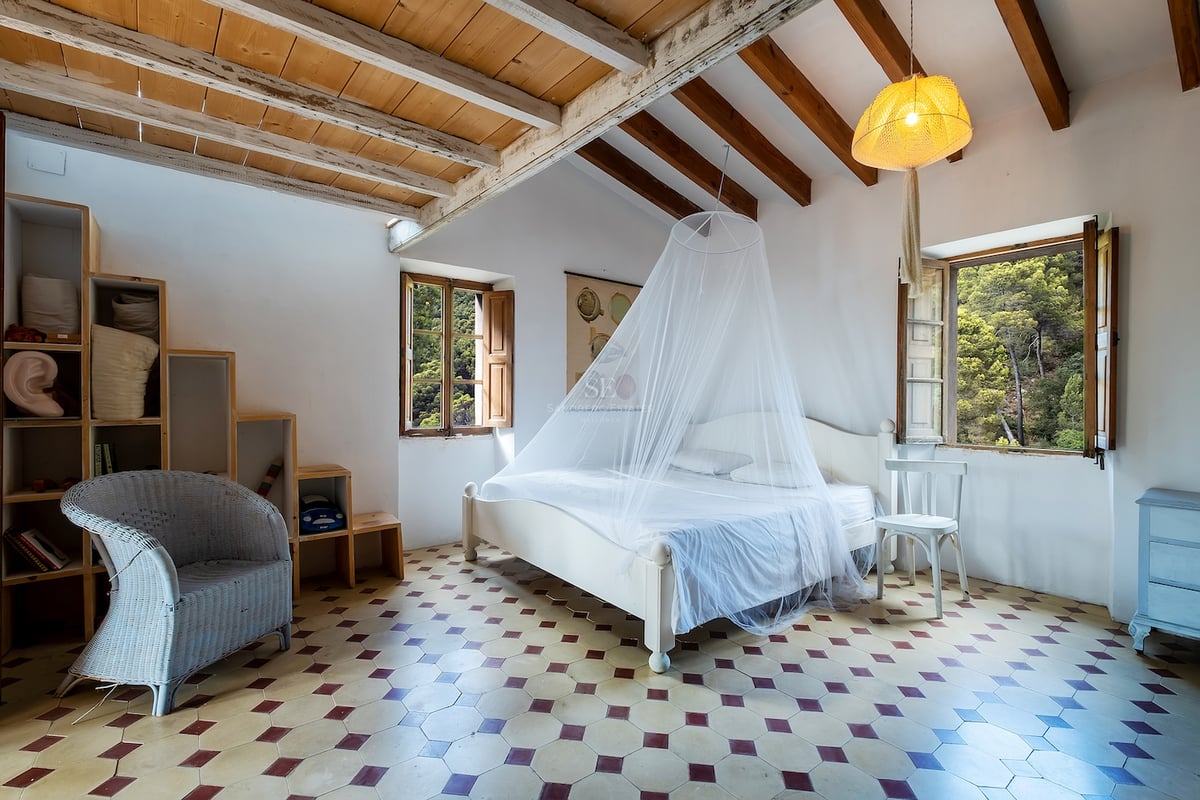 Chambre avec murs blancs, poutres en bois, sol en carrelage à motifs et lit avec moustiquaire.