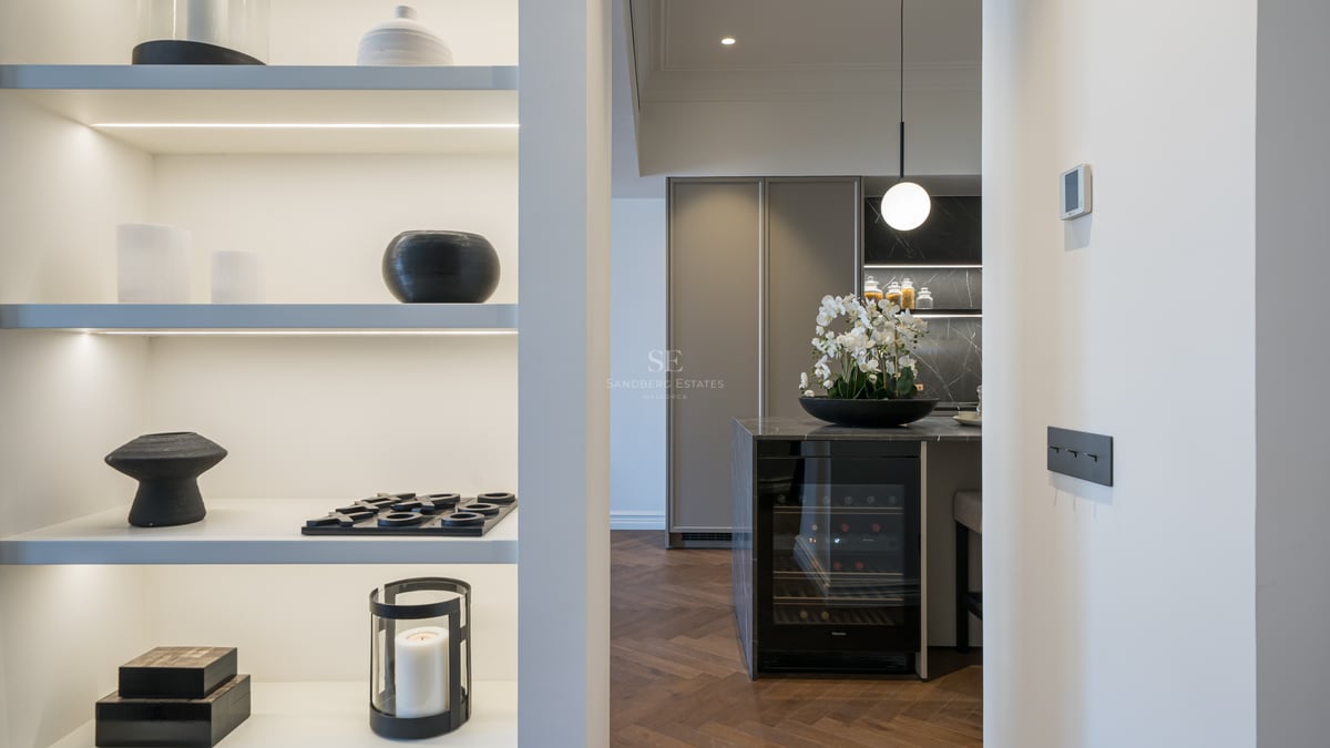 View of a modern kitchen island with built-in wine fridge, dark marble top, and herringbone wood floors.