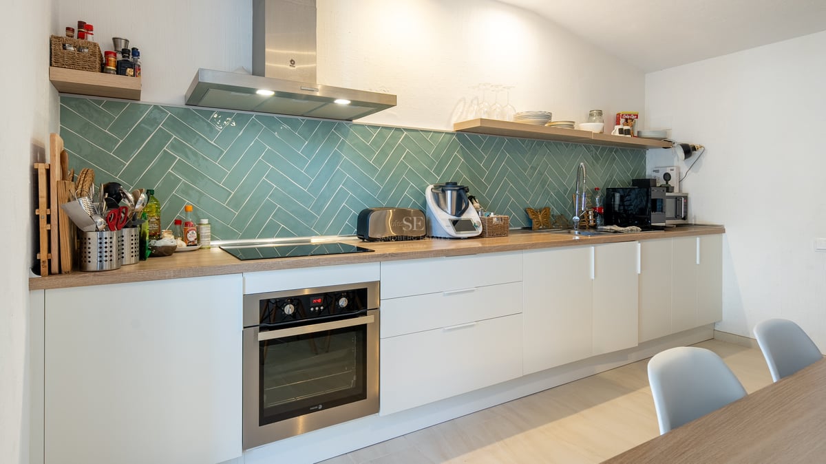 Cuisine blanche moderne avec crédence en carrelage à chevrons bleu canard, plans de travail en bois et appareils inox.