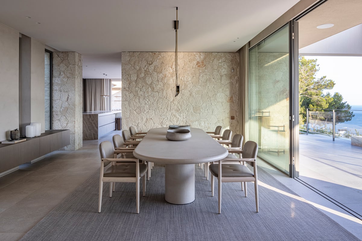 Salle à manger contemporaine avec table ovale en pierre, mur en pierre naturelle et grandes baies vitrées.