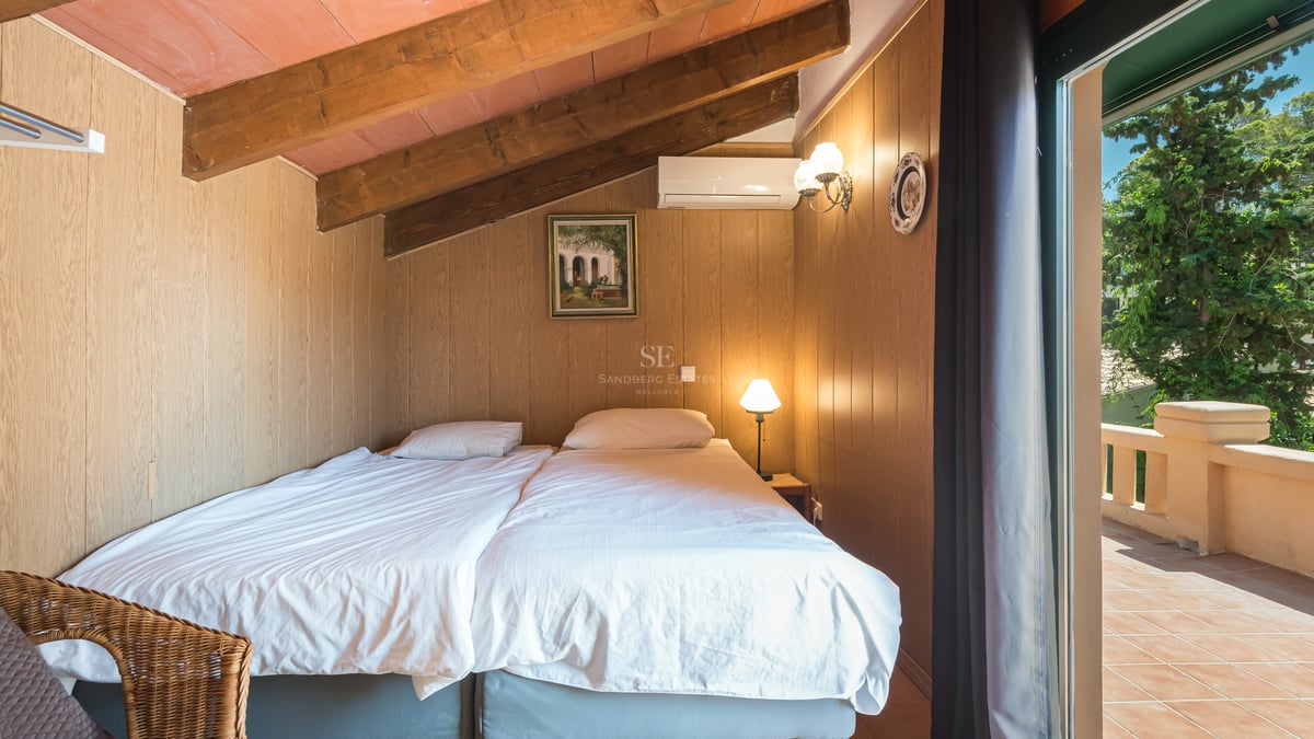 Chambre mansardée avec poutres apparentes, murs en bois et porte vitrée ouvrant sur une terrasse en terre cuite.