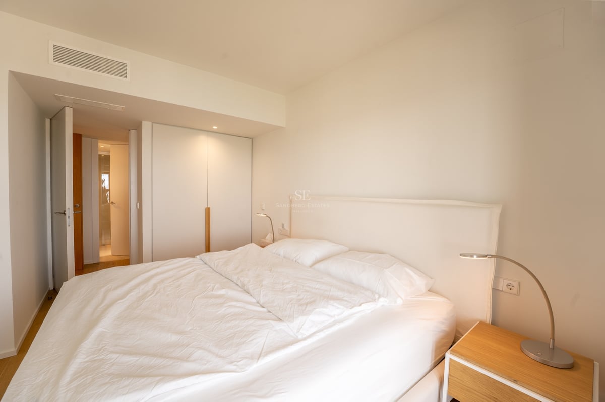 Chambre lumineuse avec grand lit, draps blancs, placard intégré et table de chevet en bois.