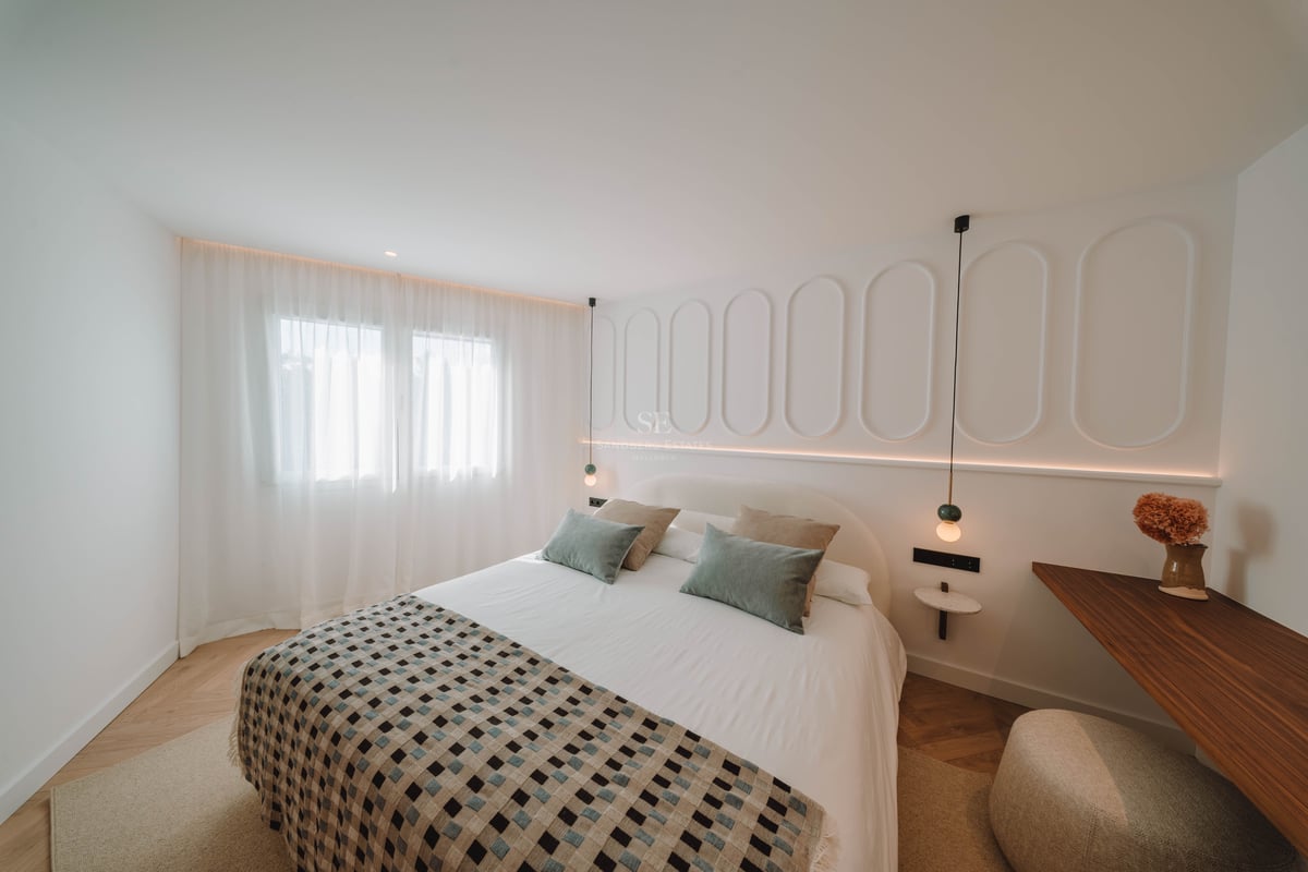 Chambre lumineuse avec un grand lit, des murs blancs décorés de moulures et un parquet en point de Hongrie.