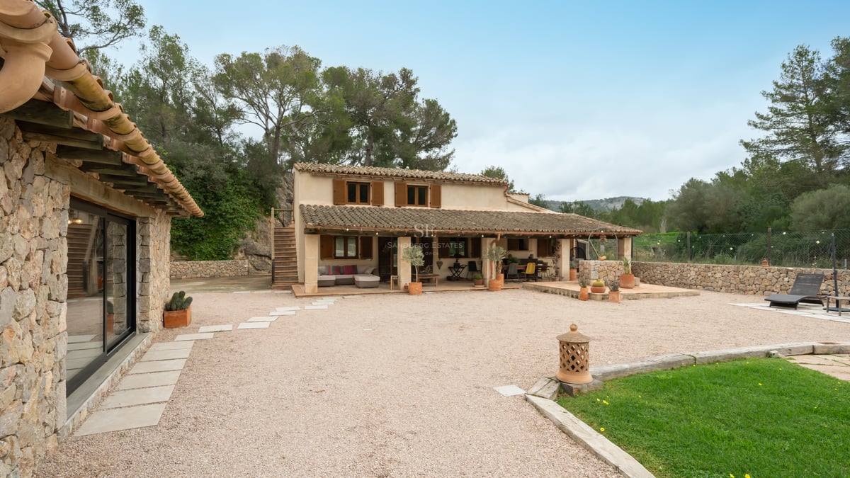 Extérieur d'une maison traditionnelle en pierre avec tuiles en terre cuite, volets en bois et cour en gravier.