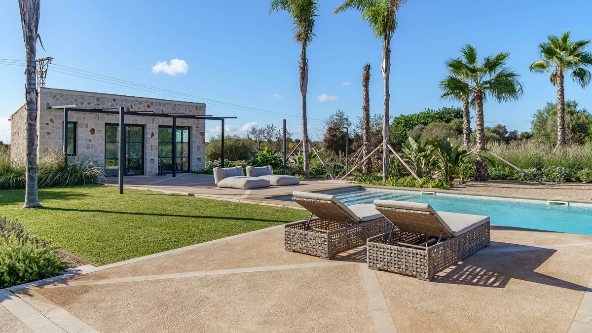 Piscine de luxe avec bains de soleil, palmiers et pavillon en pierre naturelle sous un ciel dégagé.