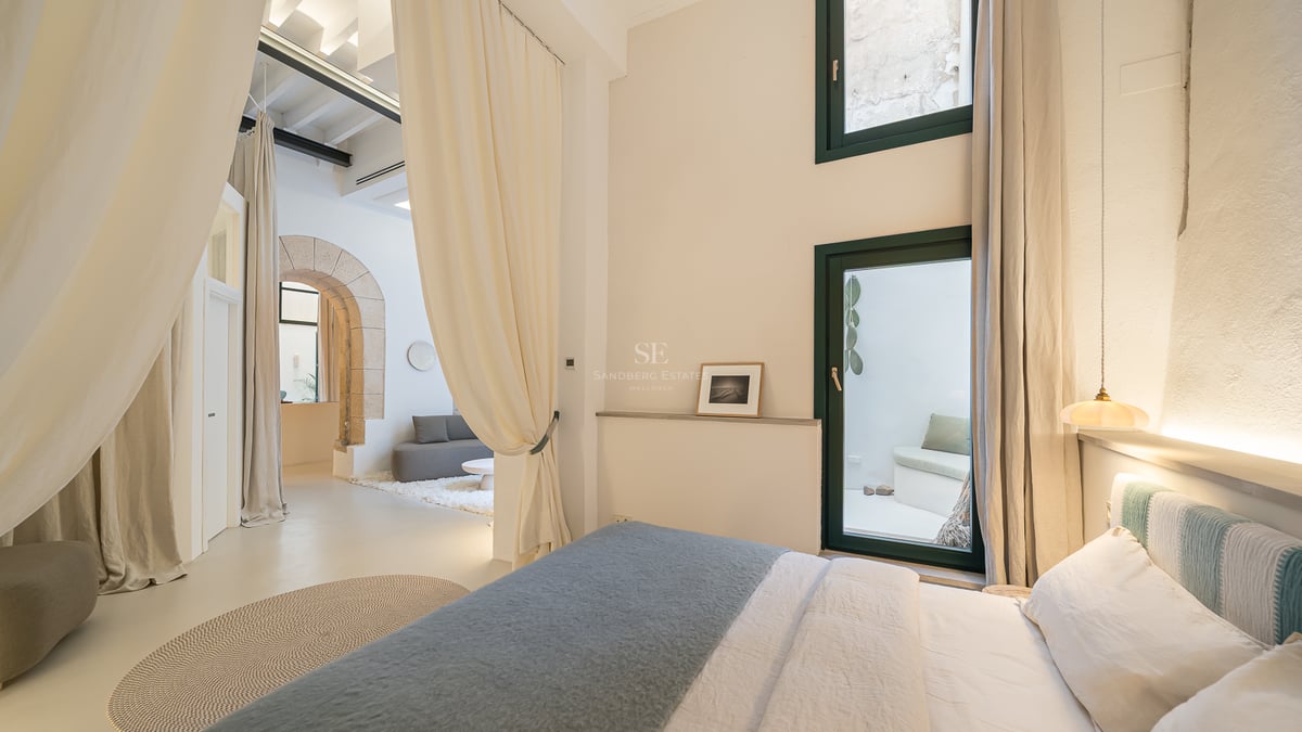 Chambre de luxe avec drapés blancs, arche en pierre historique et vue sur un salon minimaliste.