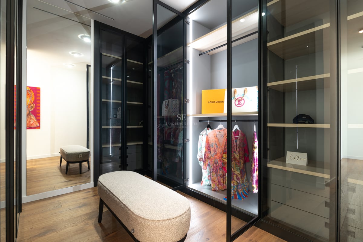 Dressing moderne avec armoires vitrées éclairées par LED, parquet et banc en tissu bouclé.
