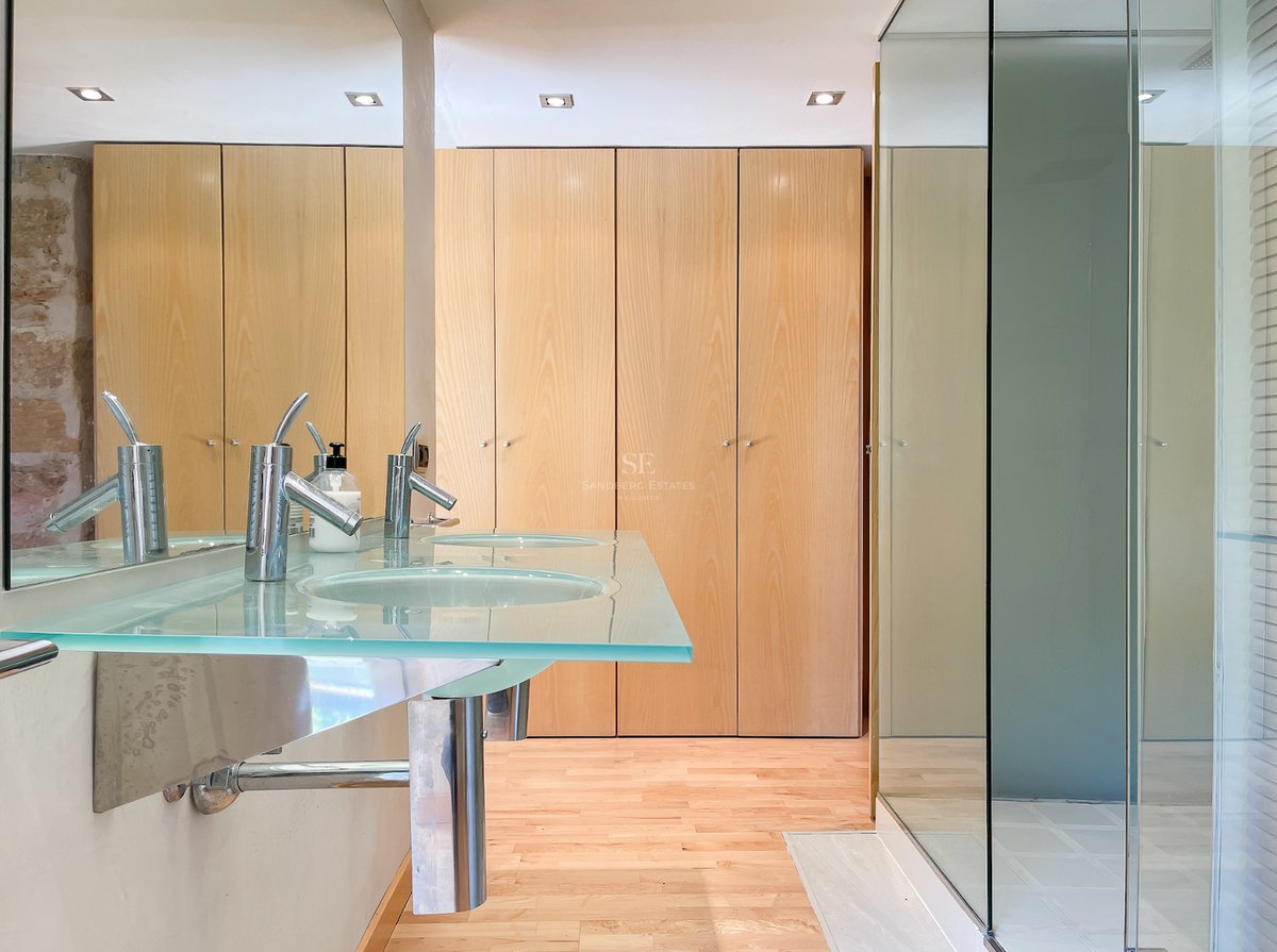 Salle de bain moderne avec plan de toilette en verre, deux vasques, robinetterie chromée et rangements en bois clair.