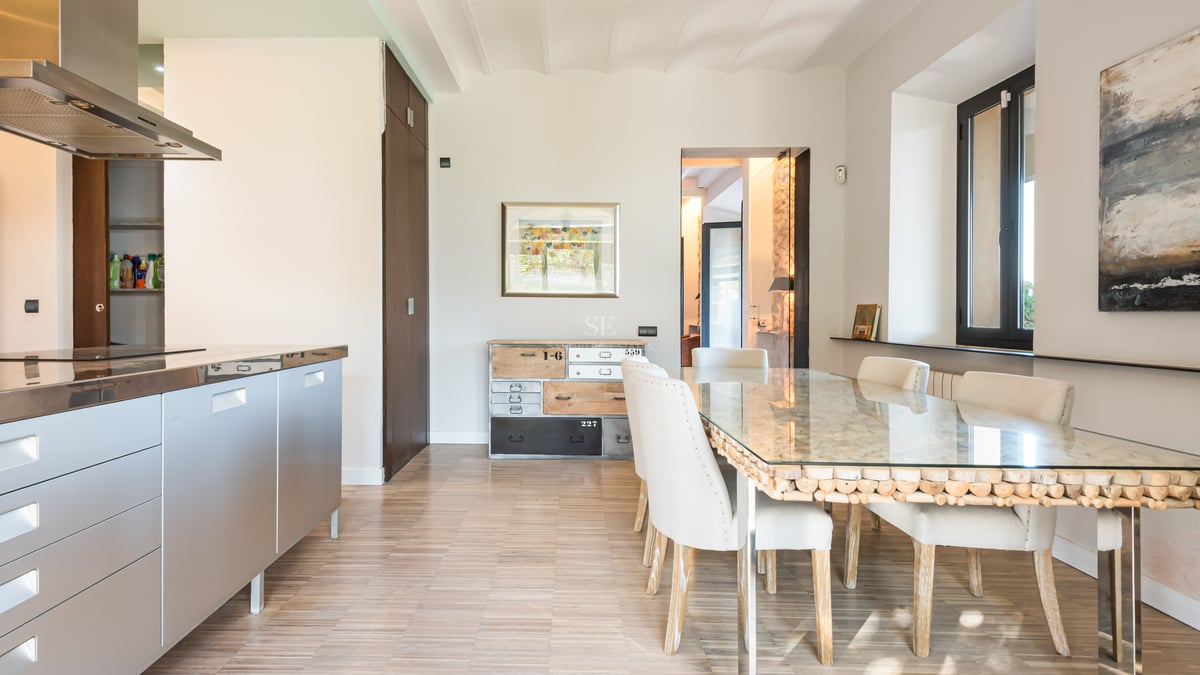 Salle à manger lumineuse avec table en verre, chaises blanches et cuisine en acier inoxydable.