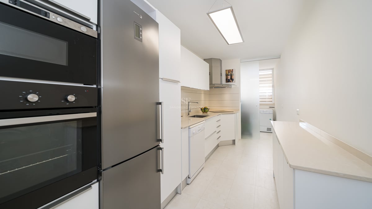 Une cuisine moderne en longueur avec des meubles blancs et des appareils en acier inoxydable.
