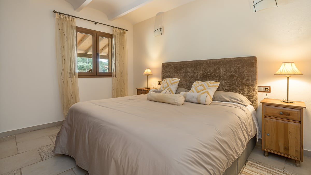 Chambre chaleureuse avec grand lit, tête de lit en velours marron, tables de chevet en bois et éclairage tamisé.
