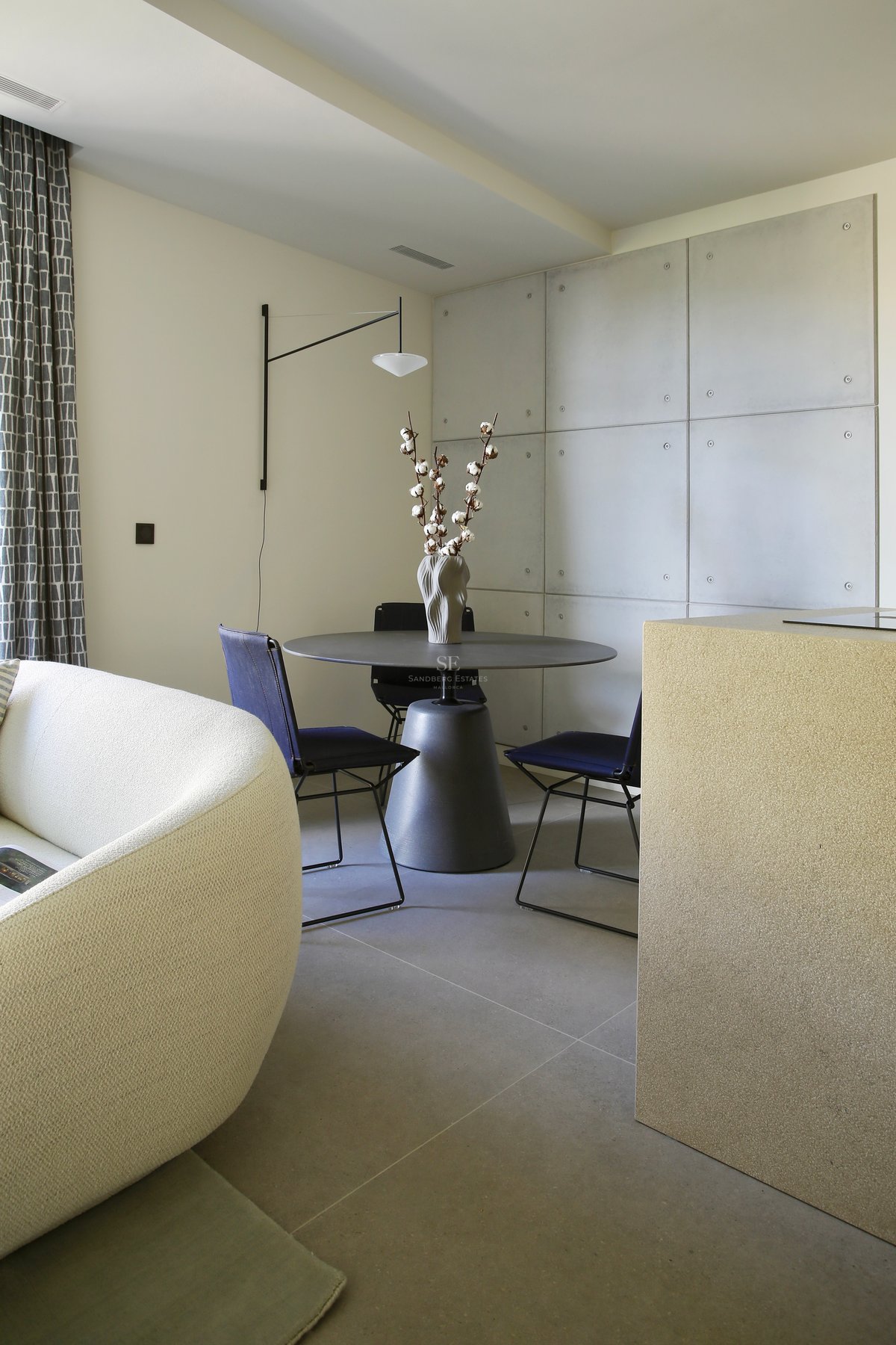 Coin repas moderne avec table ronde, chaises bleu marine et mur en panneaux de béton à côté d'un canapé courbé.