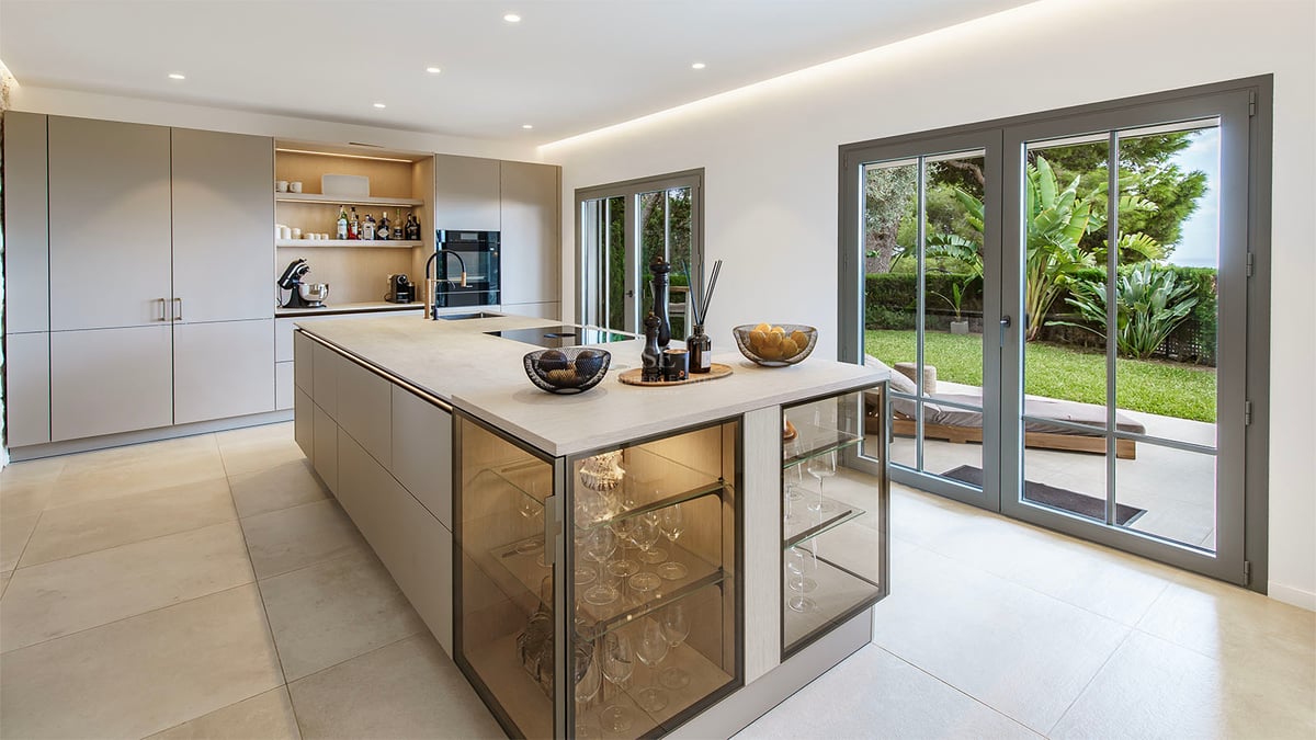 Cuisine moderne avec grand îlot, vitrines intégrées et baies vitrées ouvrant sur un jardin verdoyant.