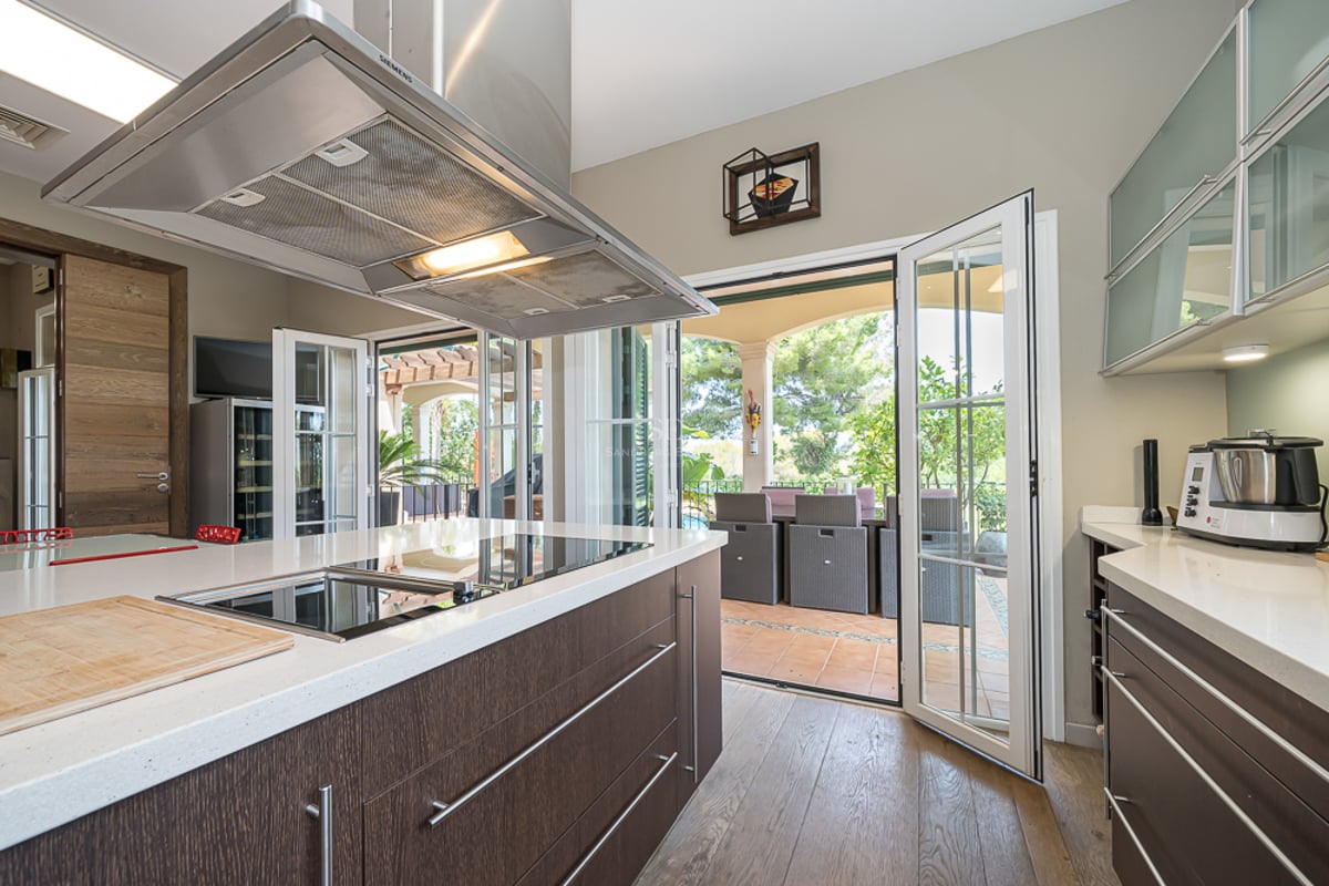 Cuisine contemporaine avec îlot en bois sombre et quartz blanc, s'ouvrant sur une terrasse dînatoire ensoleillée.