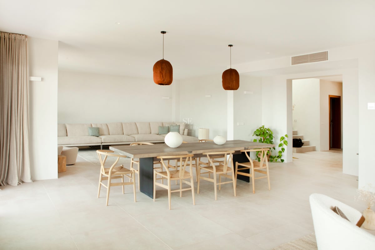 Salle à manger contemporaine lumineuse avec table en bois, chaises Wishbone et canapé neutre en arrière-plan.