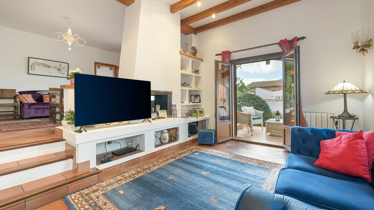 Salon avec sol en terre cuite, poutres en bois apparentes et portes ouvrant sur une terrasse ensoleillée.