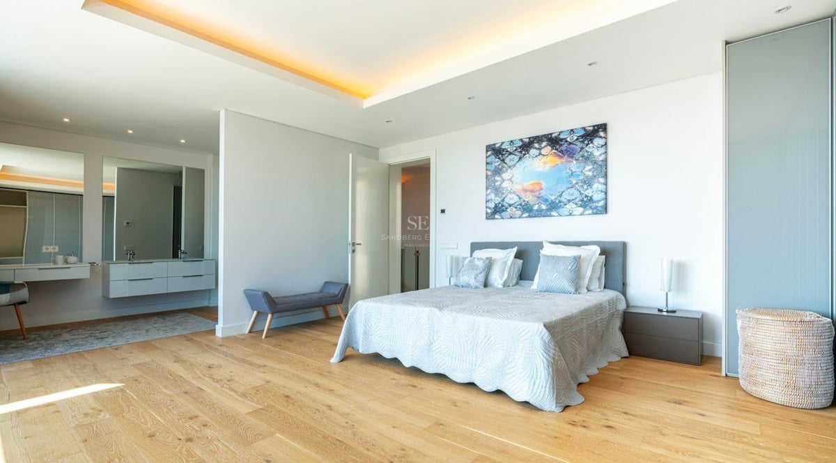 Grande chambre parentale moderne avec parquet en bois clair, lit double et espace coiffeuse attenant.