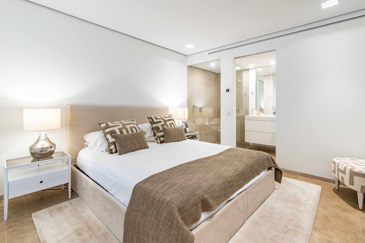 Chambre moderne aux tons neutres, lit rembourré et salle de bains vitrée avec sol en pierre naturelle.